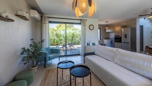 Un moderno salón con un sofá, dos mesitas auxiliares, una planta en maceta y un amplio ventanal con vistas al exterior.