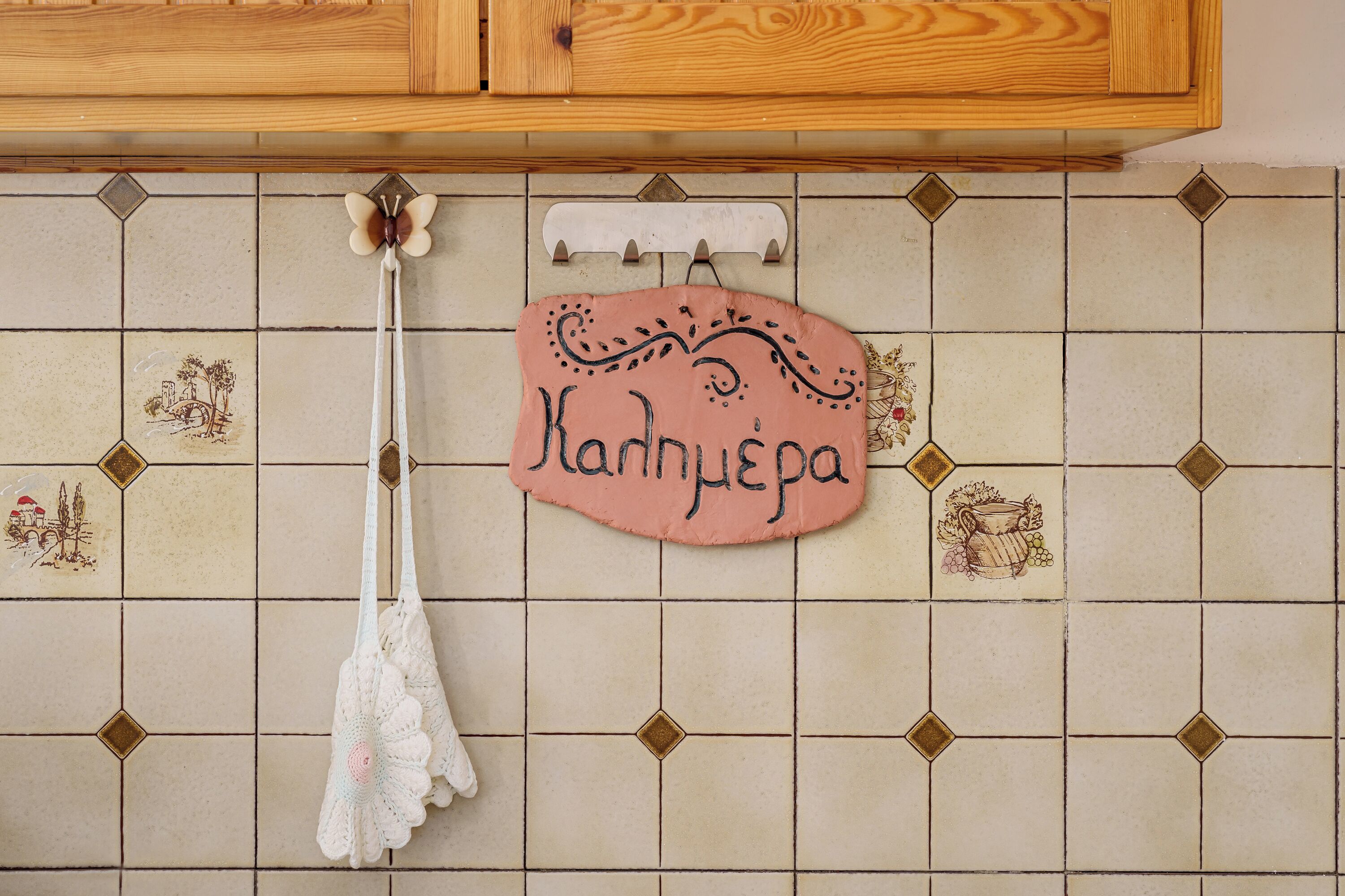 A kitchen with a tiled backsplash, a hanging white cloth, and a pink sign with the name "Kandhypega".