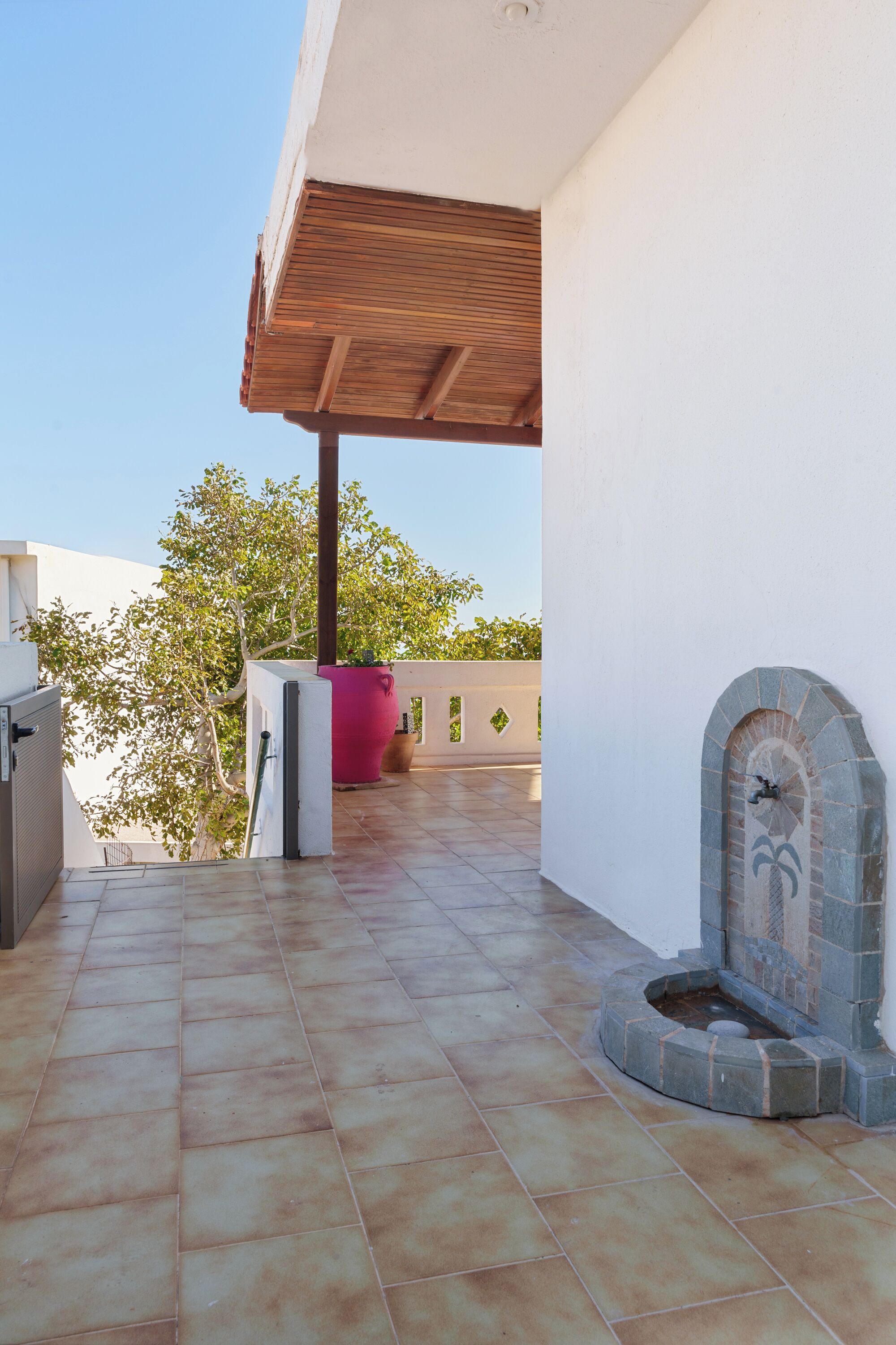A covered outdoor area with tiled flooring, a stone fountain, and a potted plant.