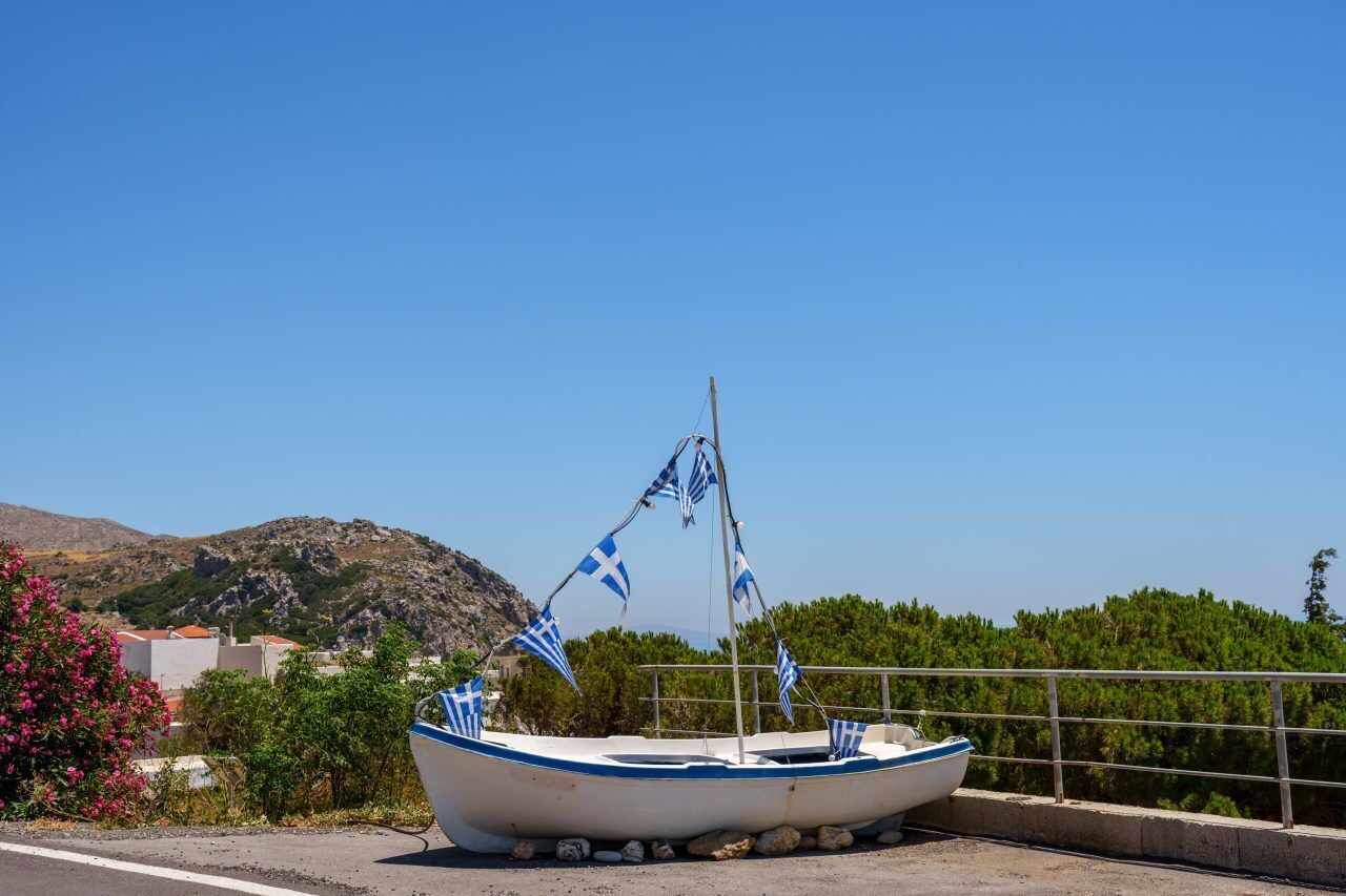 Um barco com bandeiras, estacionado perto de uma estrada com montanhas ao fundo.