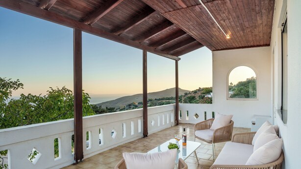 A covered outdoor seating area with wicker furniture and a table, overlooking a scenic landscape. - Libyan Horizon Seaview (Rethymno)