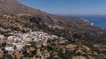 A coastal village with white buildings, a mountainous backdrop, and a view of the sea.