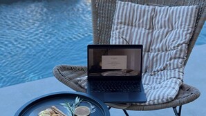 A wicker chair with a laptop and a tray with pastries and a drink by a poolside. - Libyan Horizon Seaview (Rethymno)