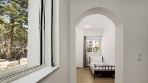 A bedroom with a bed, a window, and a view of trees and a building outside. - Libyan Horizon Seaview (Rethymno)