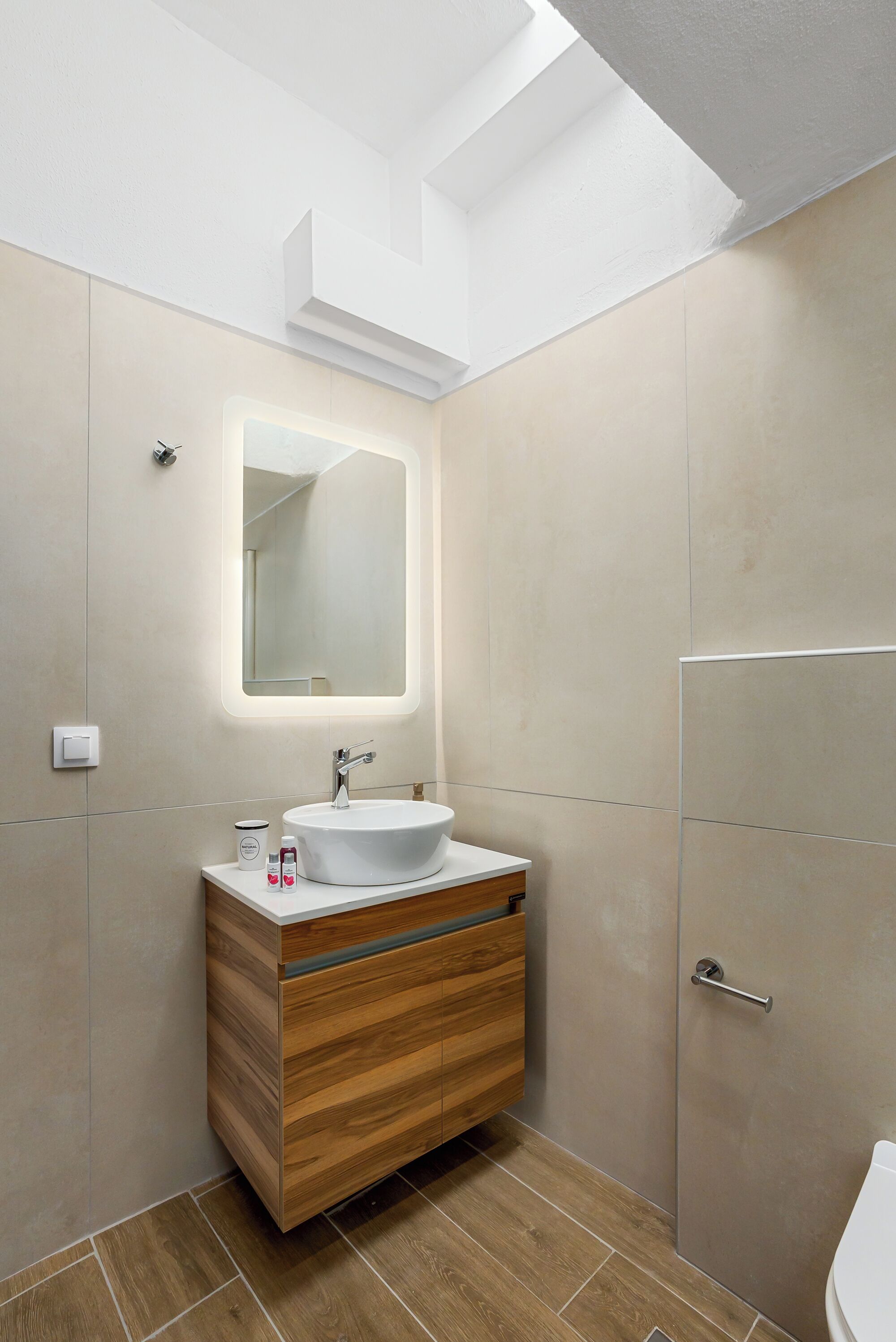 Ein modernes Badezimmer mit Dachfenster, einem Holzkosmetikschrank, einem weißen Waschbecken und einem großen Spiegel.