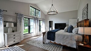 A bedroom with a large bed, a TV, a dresser, and a window with curtains.