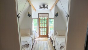 Un couloir avec deux lits de chaque côté, un plancher en bois et une porte donnant sur une pièce lumineuse avec vue sur la verdure.