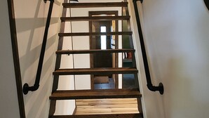 Un escalier en bois avec des rampes en métal mène à une pièce d’où l’on peut admirer les arbres à travers une fenêtre.