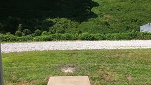 A covered outdoor area with a gravel path, green grass, and dense trees in the background. - 3 bedroom, 3 bath home in Matewan, WV. 1 mile from the Devil Anse trailhead. (Matewan)