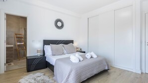 A neatly arranged bedroom with a bed, bedside tables, a wall-mounted mirror, and a door. - Casa da Torre in Portimão (Portimão)