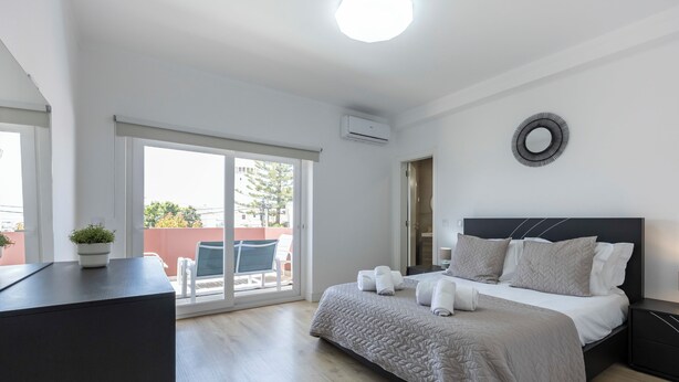 A modern bedroom with a large bed, a potted plant, and a view through a sliding glass door. - Casa da Torre in Portimão (Portimão)