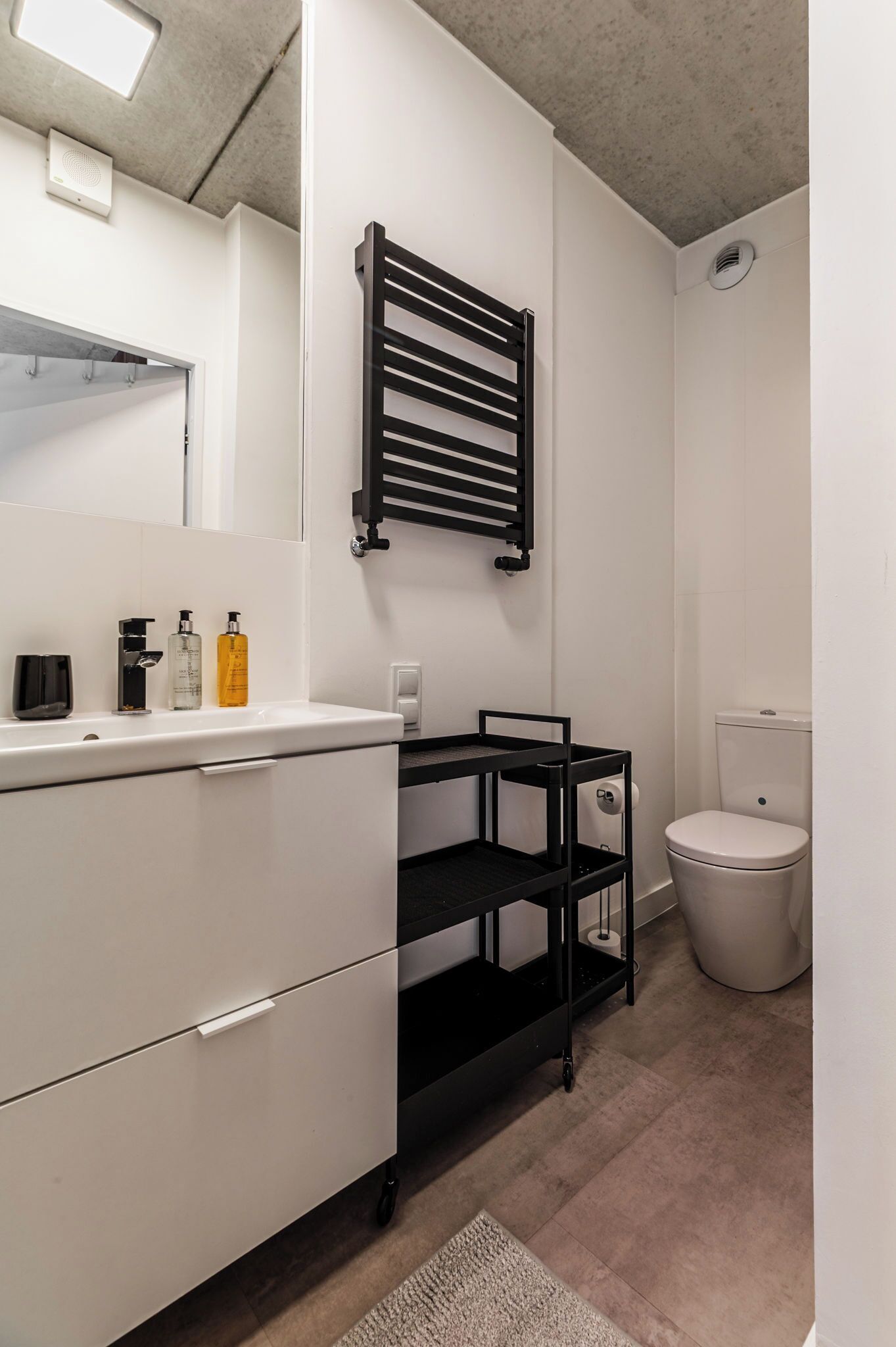 A modern bathroom with a white vanity, black towel rack, and a toilet.
