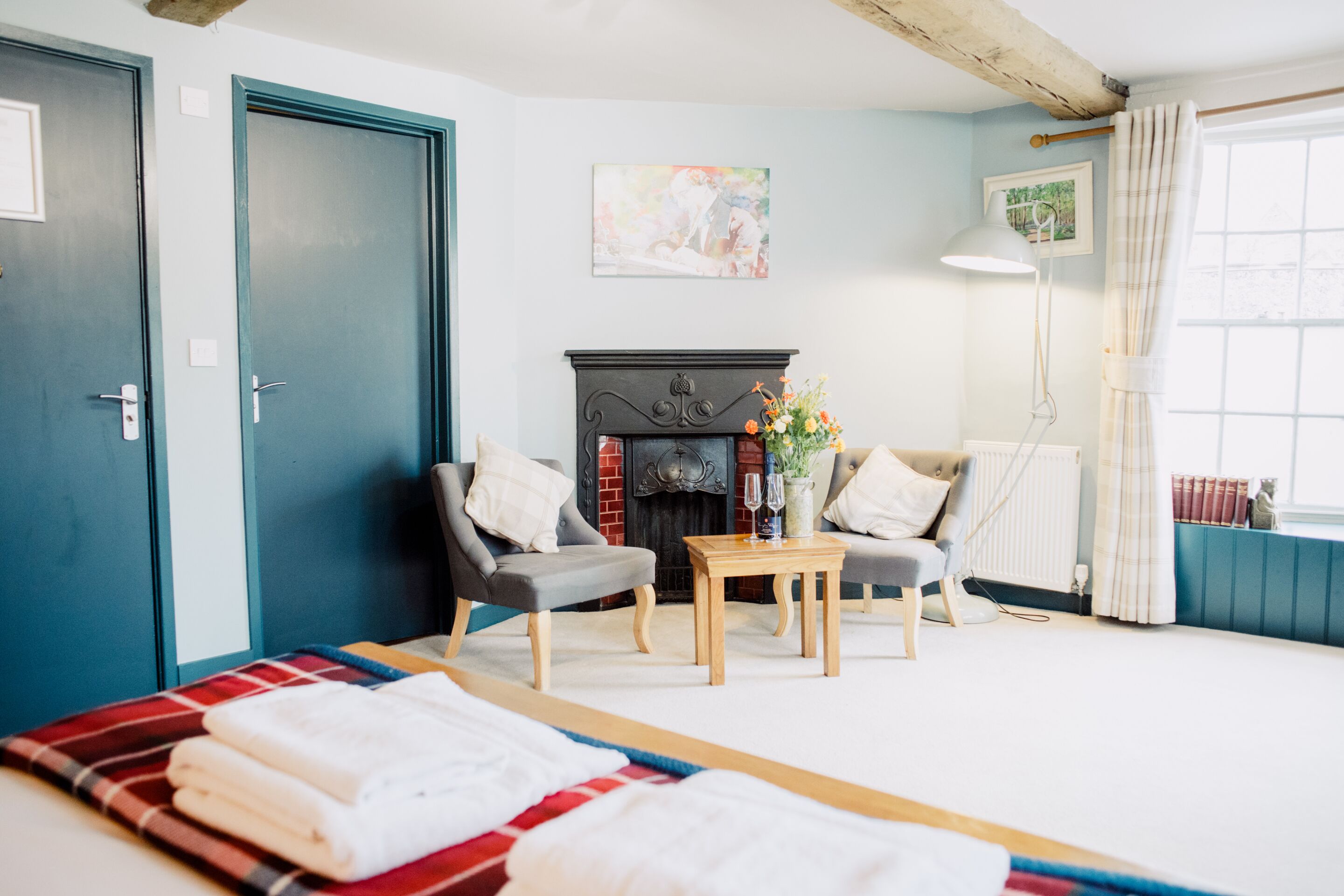Una habitación con cama, dos sillones, una mesa, chimenea y ventana con cortinas.