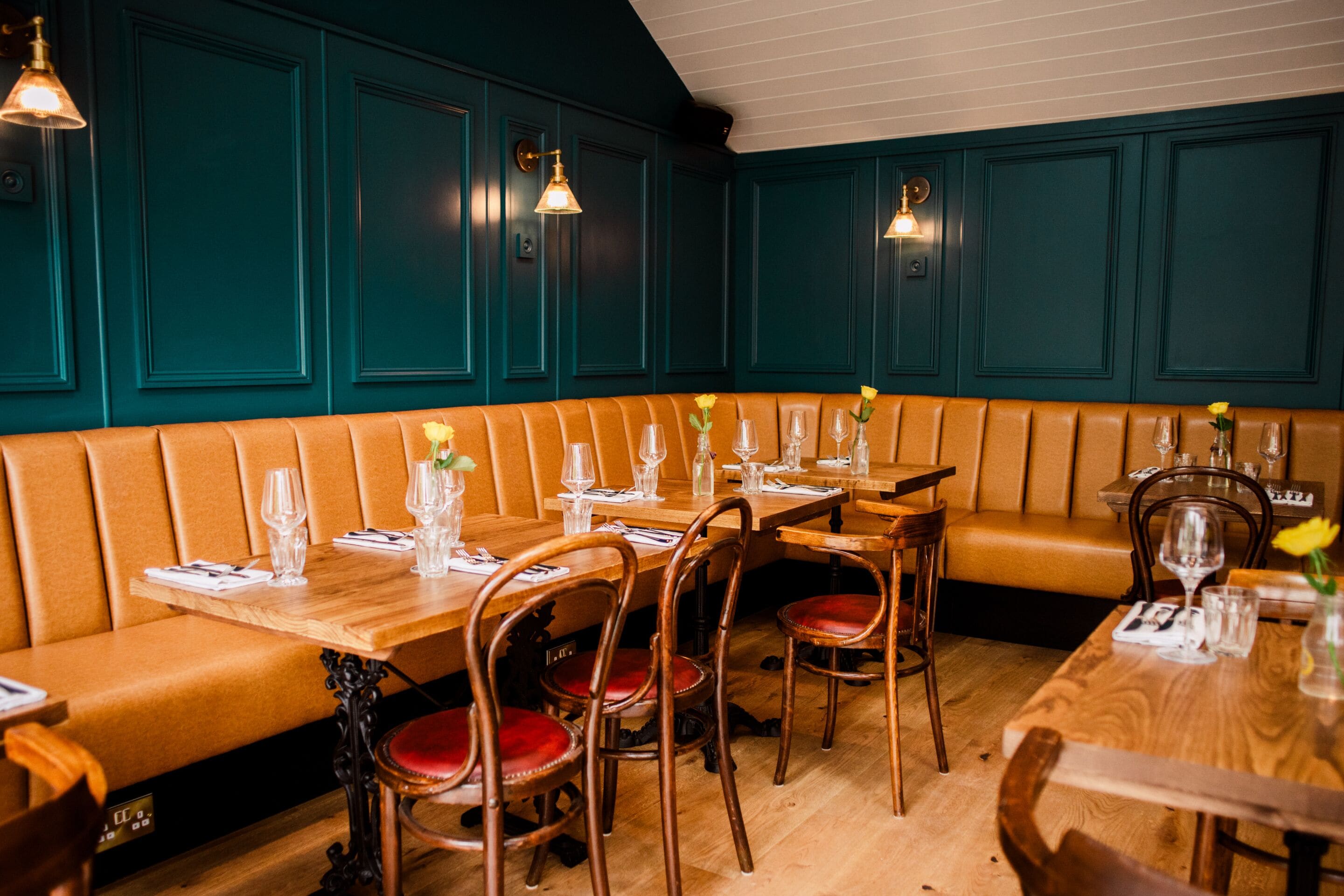 A restaurant with wooden tables, red cushioned booths, and teal walls.