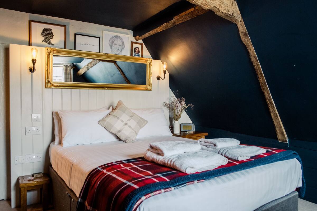 Un dormitorio con cama, espejo, luces fijadas a la pared, mesita de noche y mesilla.
