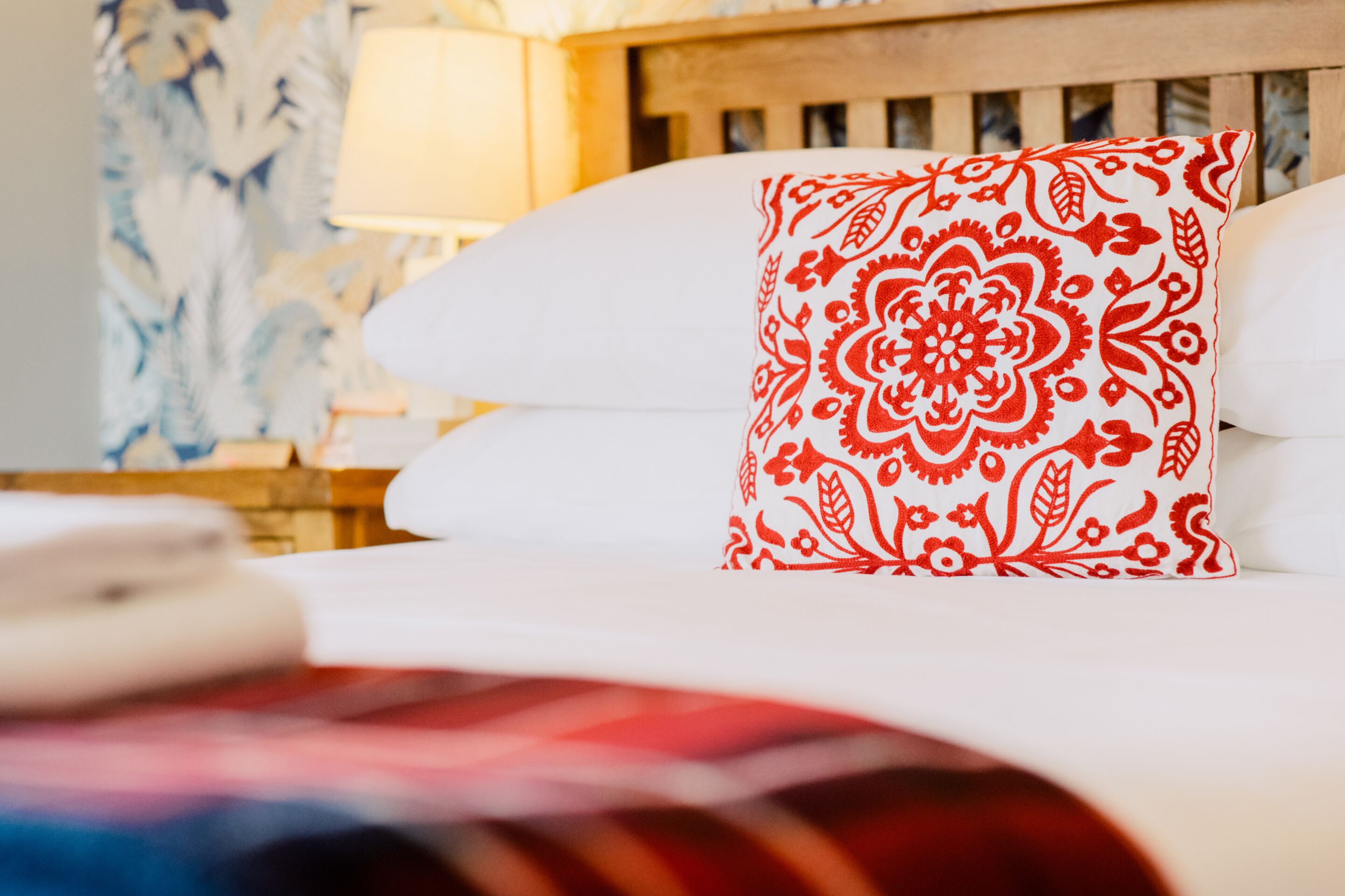 A bed with a white pillow and a red patterned pillow.