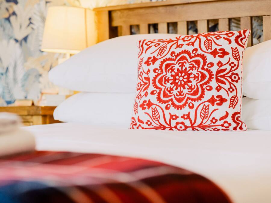 A bed with a white pillow and a red patterned pillow.