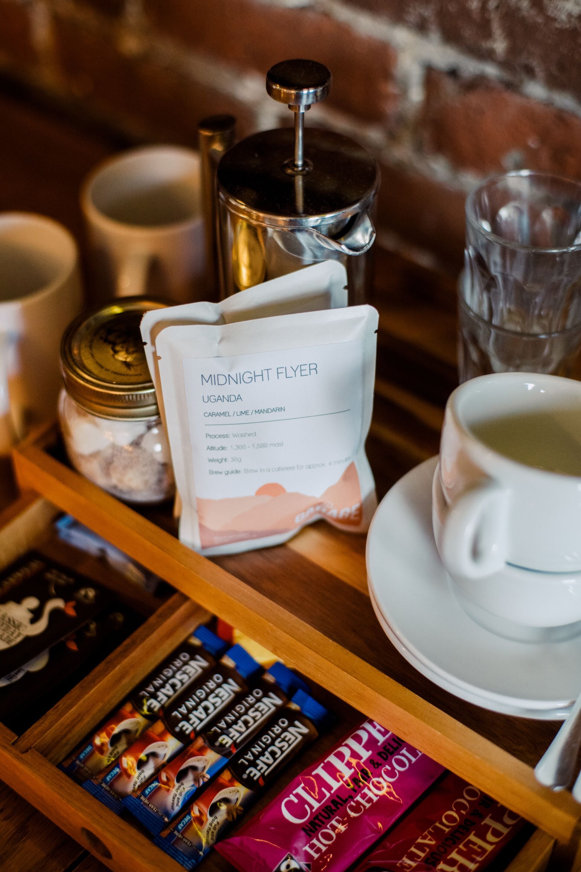 Una bandeja con una cafetera, un paquete de Midnight Flyer Uganda, una taza de té y una bandeja de barras de chocolate.