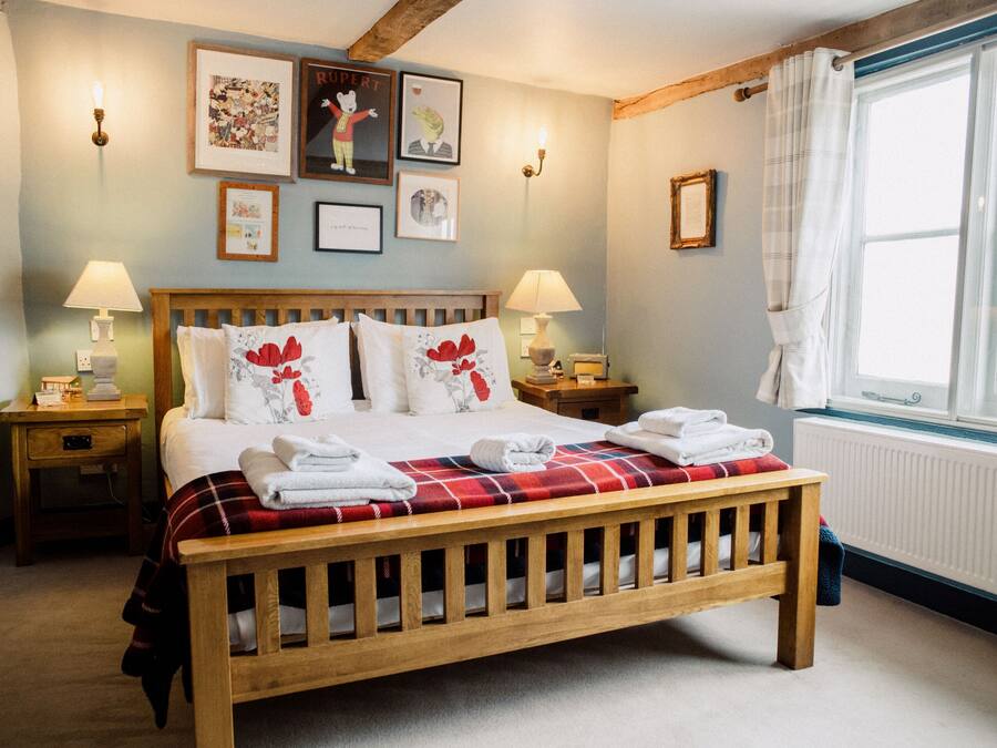 A bedroom with a wooden bed, two bedside tables with lamps, a window with curtains, and wall art.