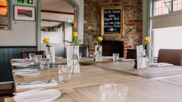 A restaurant with wooden tables, yellow roses in vases, and a brick wall with a chalkboard menu.