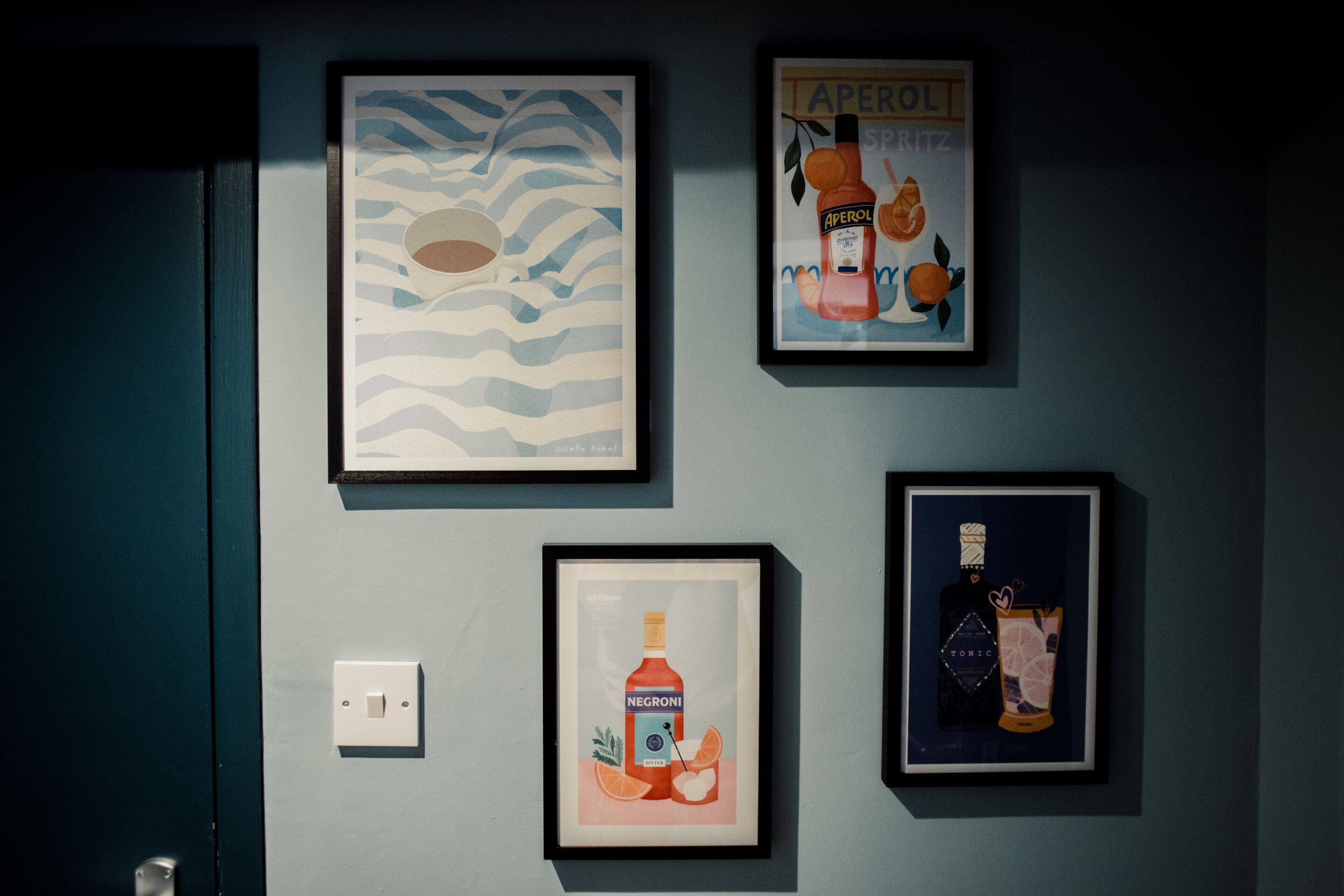 A wall with four framed artworks, a light switch, and a door.