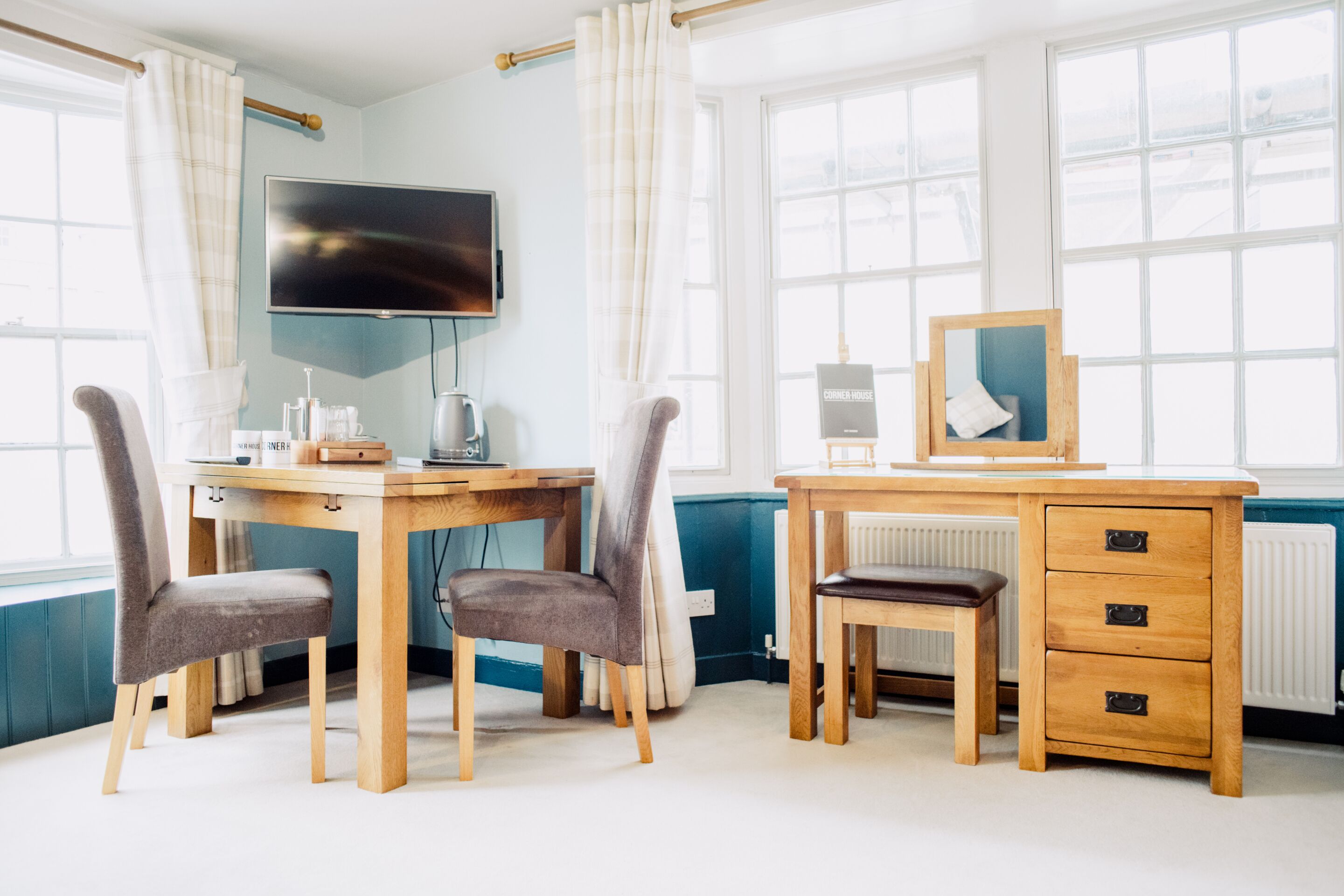 A room with a wooden desk, two chairs, a television, a radiator, and large windows.