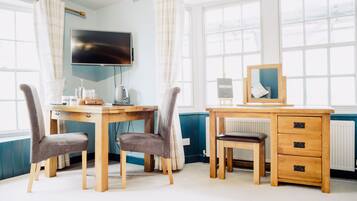 A room with a wooden desk, two chairs, a television, a radiator, and large windows.