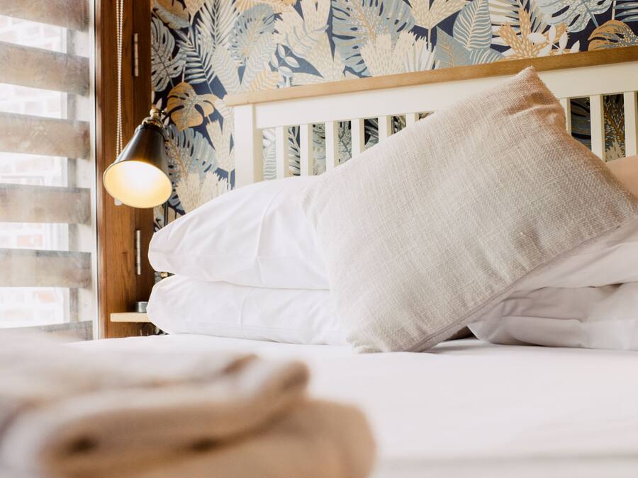 A bed with white bedding, a wooden headboard, and a wall with a leafy pattern.