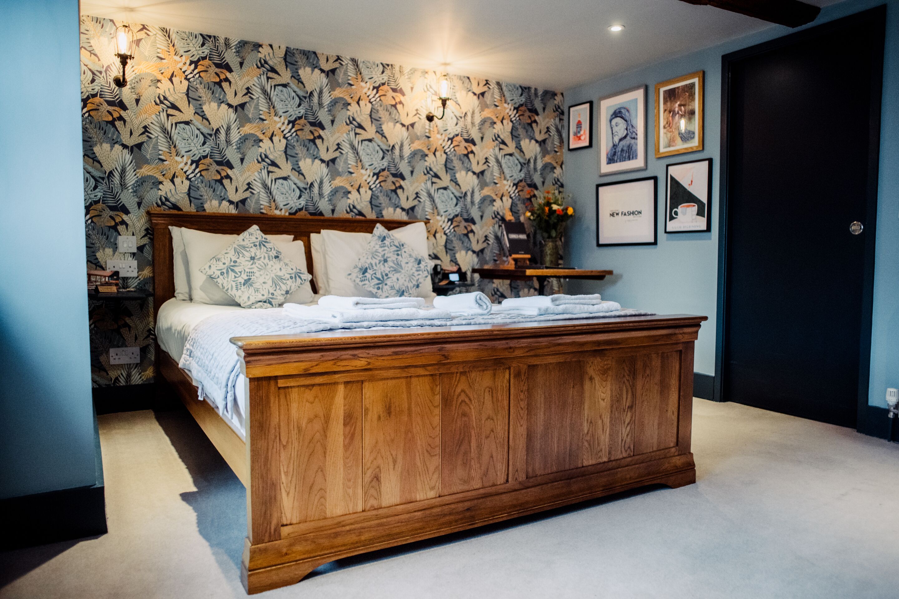 A bedroom with a wooden bed, floral wallpaper, and framed pictures on the wall.