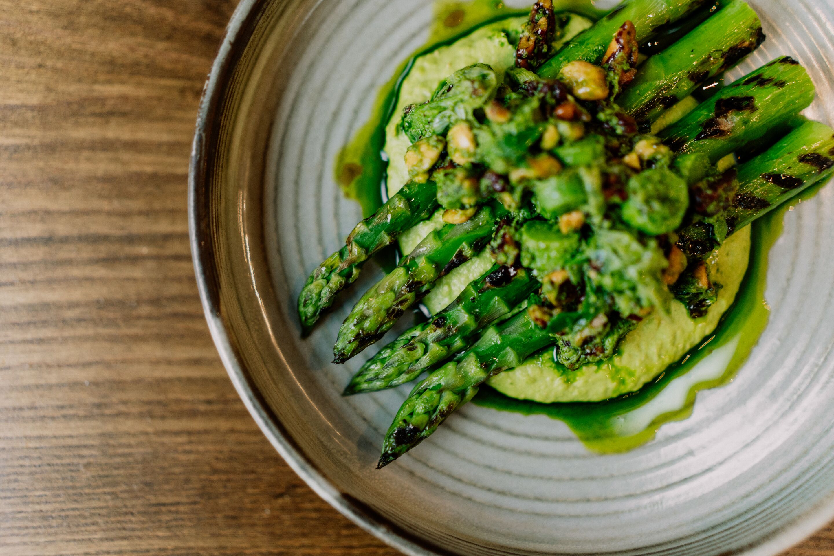 A plate of grilled asparagus with a green sauce and nuts.
