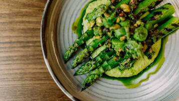 A plate of grilled asparagus with a green sauce and nuts.