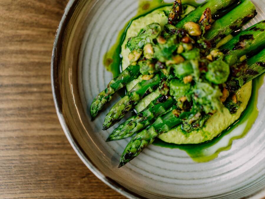 A plate of grilled asparagus with a green sauce and nuts.