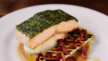 A dish with a piece of fish, bacon, and a creamy sauce on a plate.