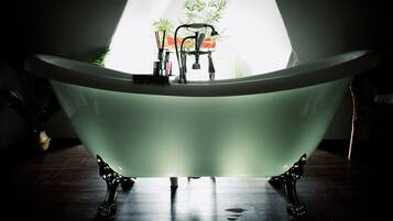 Une baignoire sur pied dans une pièce à la lumière tamisée, avec une plante en arrière-plan.