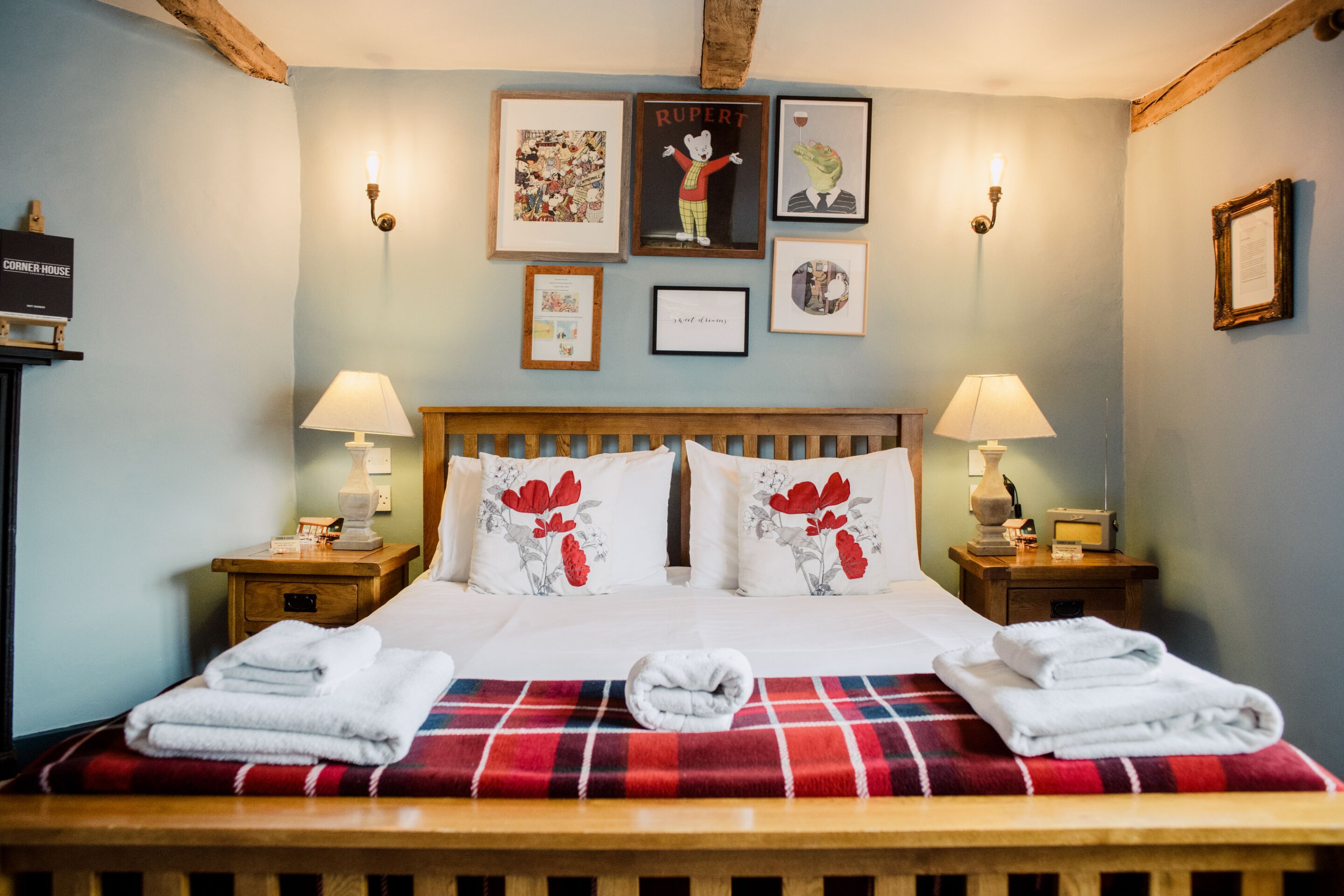 A neatly made bed with a plaid blanket, two bedside tables with lamps, and framed pictures on the wall.