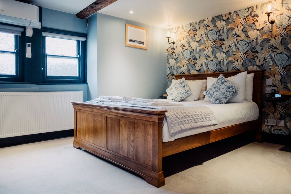 Un dormitorio con cama de madera, un radiador, una ventana y un papel tapiz estampado.