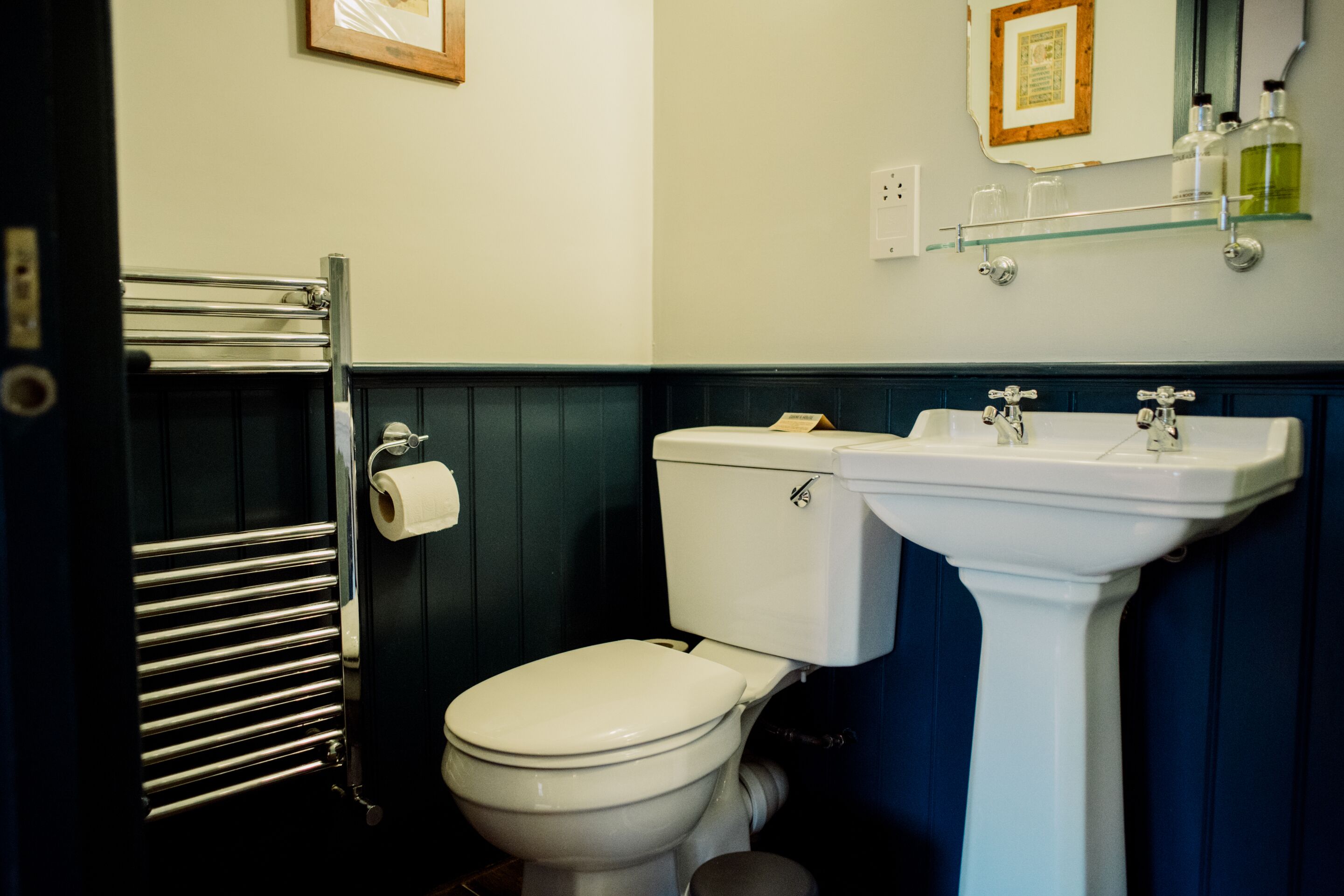 Un baño con inodoro, lavamanos y repisa de vidrio sobre el lavamanos.
