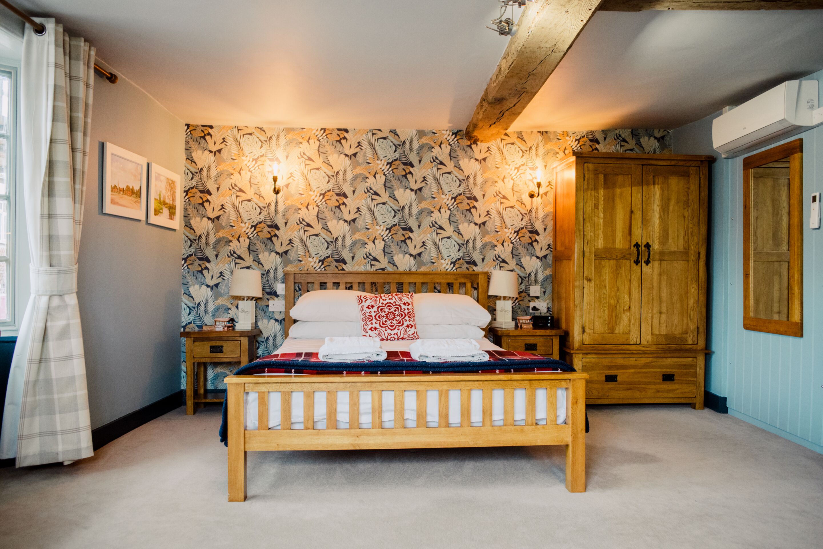 A bedroom with a wooden bed, a nightstand, a wardrobe, and a patterned wallpaper.