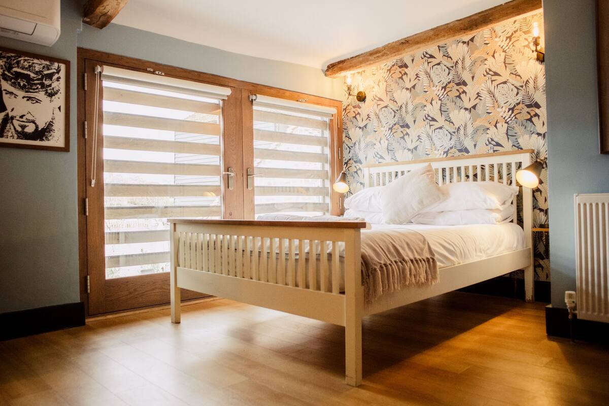 Un dormitorio con cama de madera, cabecera blanca, banco de madera, radiador y una puerta con persianas.