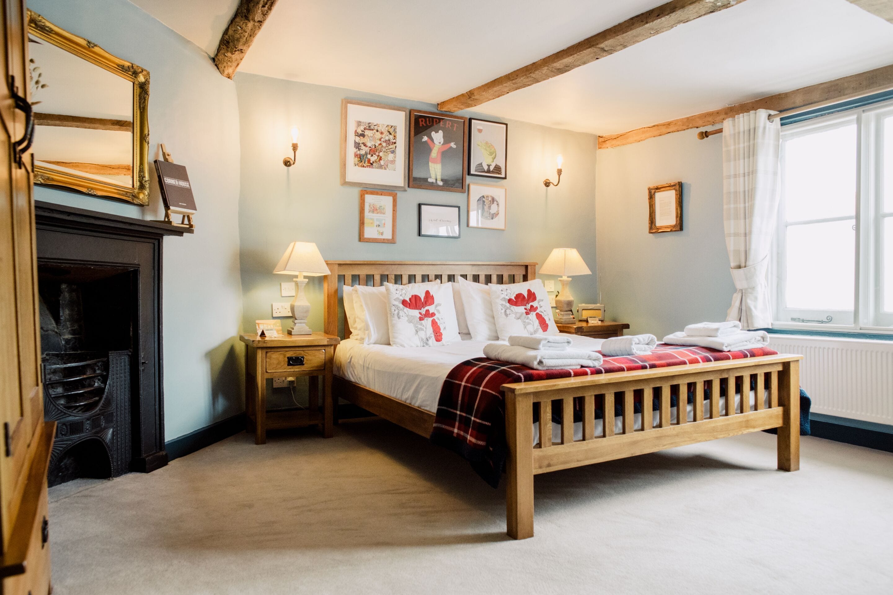 A bedroom with a wooden bed, bedside tables, a fireplace, and framed pictures on the wall.