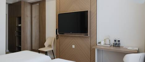 A hotel room with two beds, a TV mounted on a wooden panel, a desk with a chair, and a trash bin.