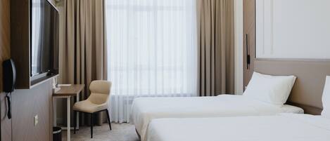 A hotel room with two beds, a desk, a chair, a TV, and a window with curtains.