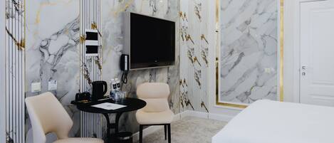 Habitación de hotel con cama, televisor, escritorio y dos sillas, además de paredes con diseño de mármol.