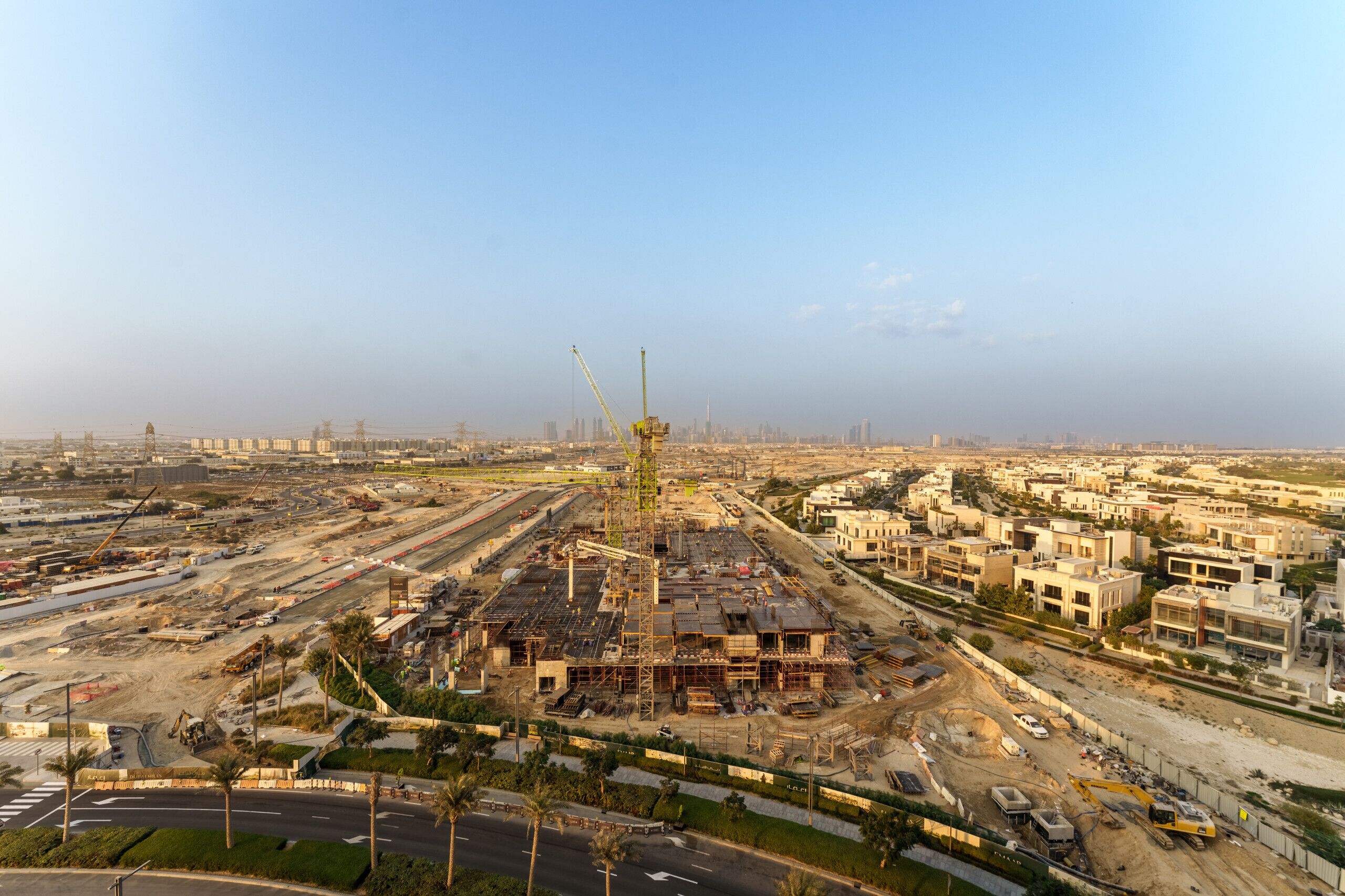 An aerial view of a construction site with a large crane, surrounding buildings, and roads.