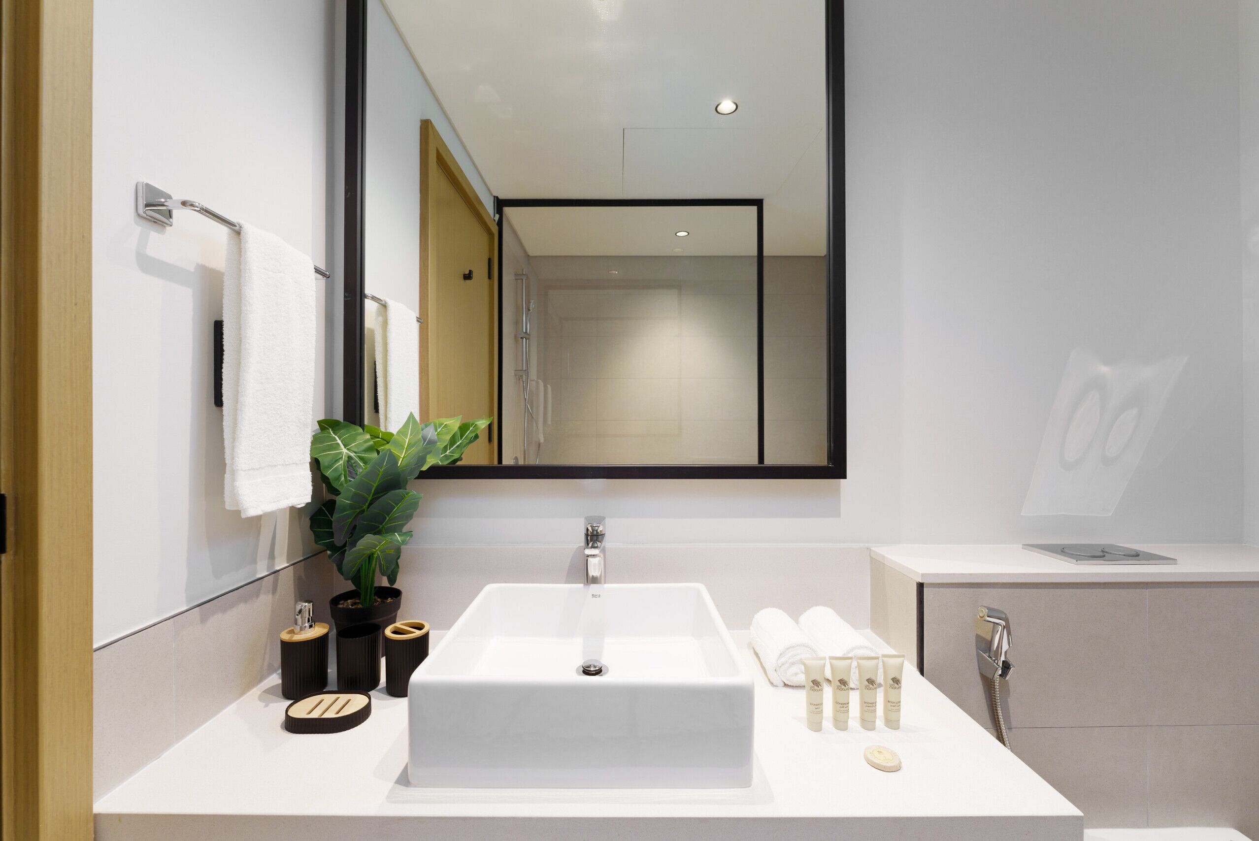 Een moderne badkamer met een grote spiegel, een witte wastafel en een potplant.