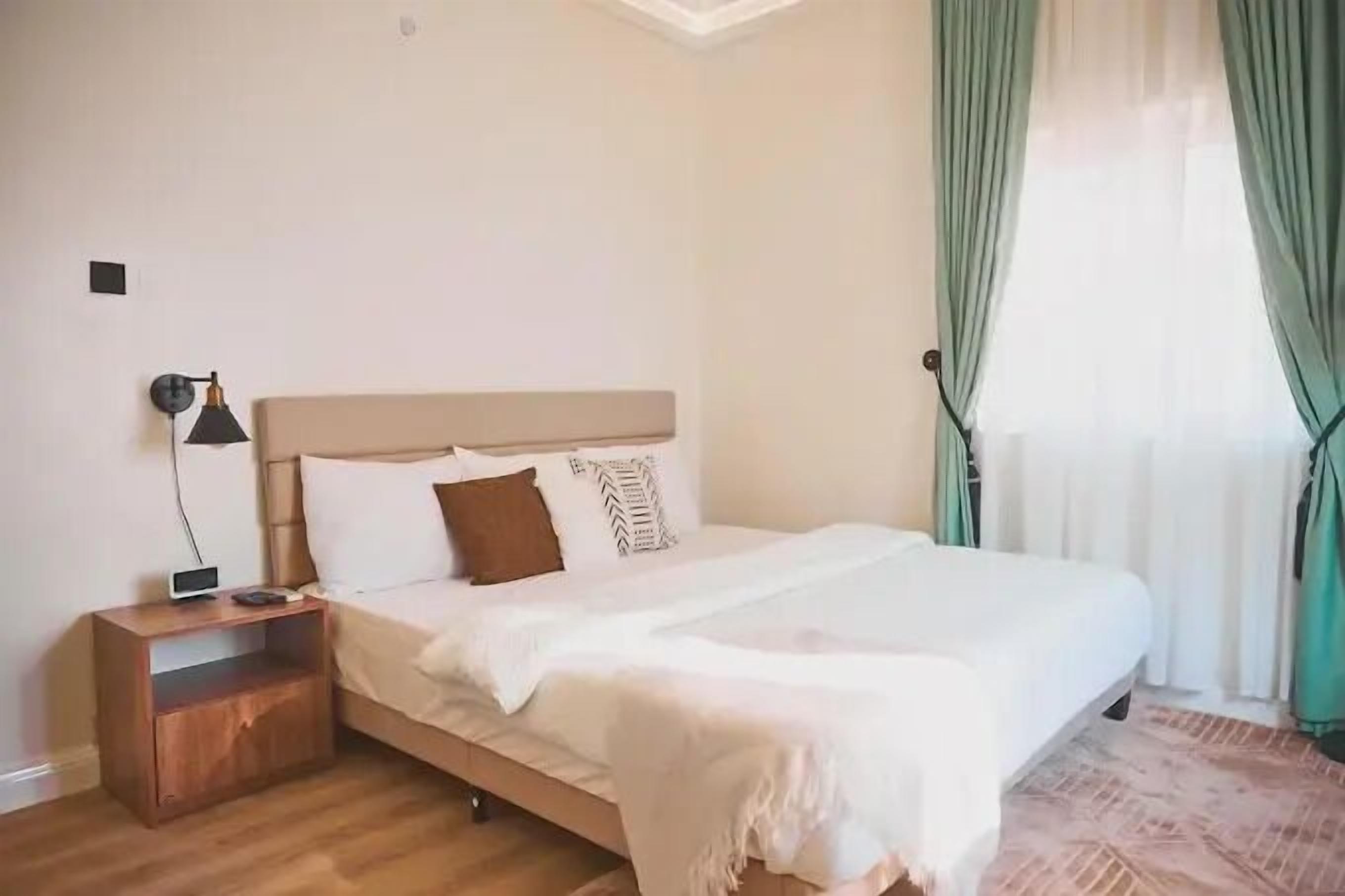 Un dormitorio con cama, mesita de noche, lámpara y ventana con cortinas.
