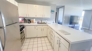 A modern kitchen with white cabinets, a stainless steel refrigerator, a coffee maker, and a sink. - Aloha Living at Waikiki Lanais | Pool + Gym (Honolulu)