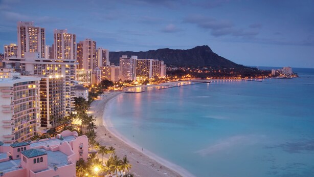 A coastal cityscape with high-rise buildings, a beach, and a mountain in the background. - Aloha Living at Waikiki Lanais | Pool + Gym (Honolulu)