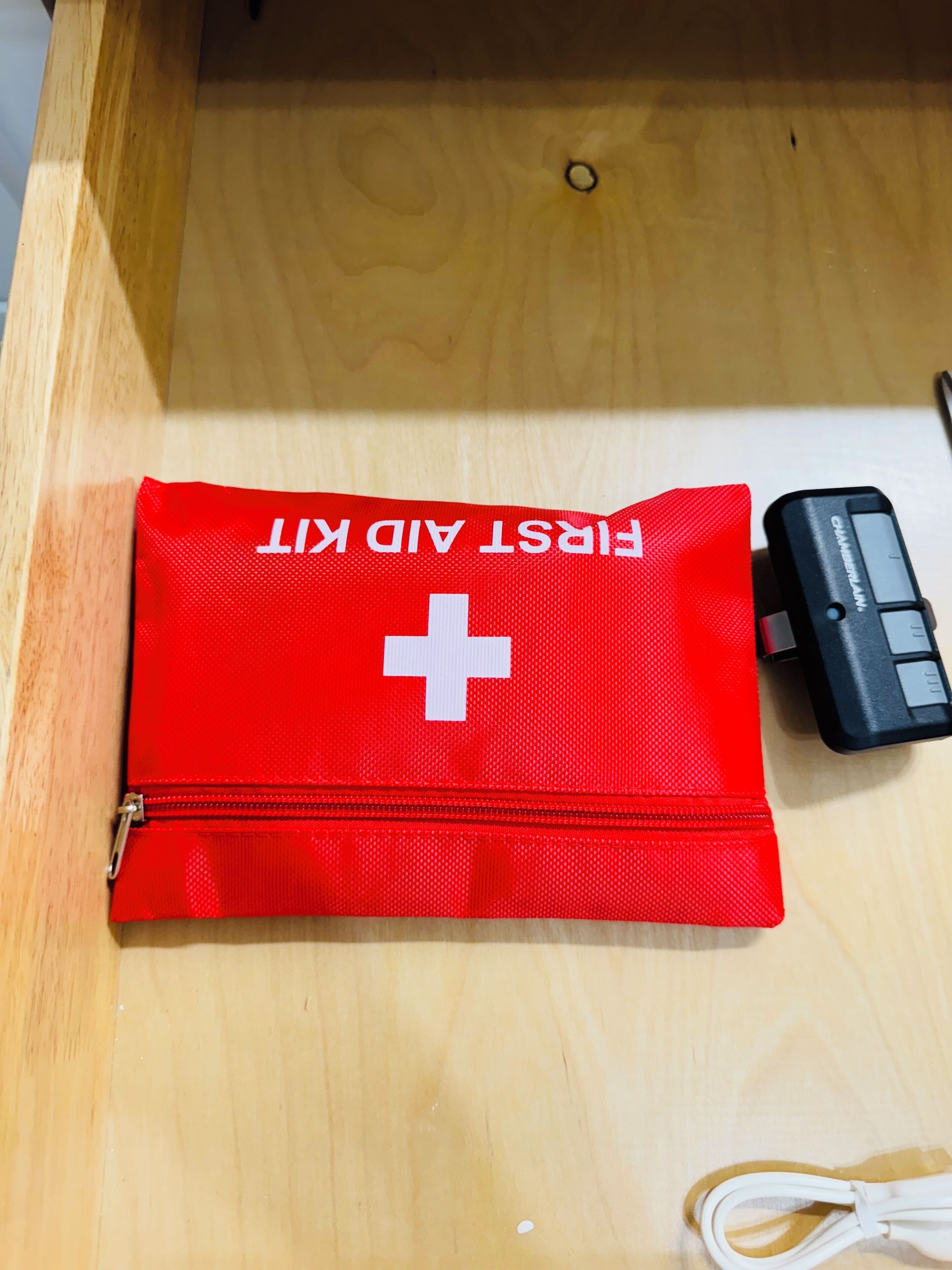 A red first aid kit with a white cross, a black charger, and a white charging cable on a wooden surface.