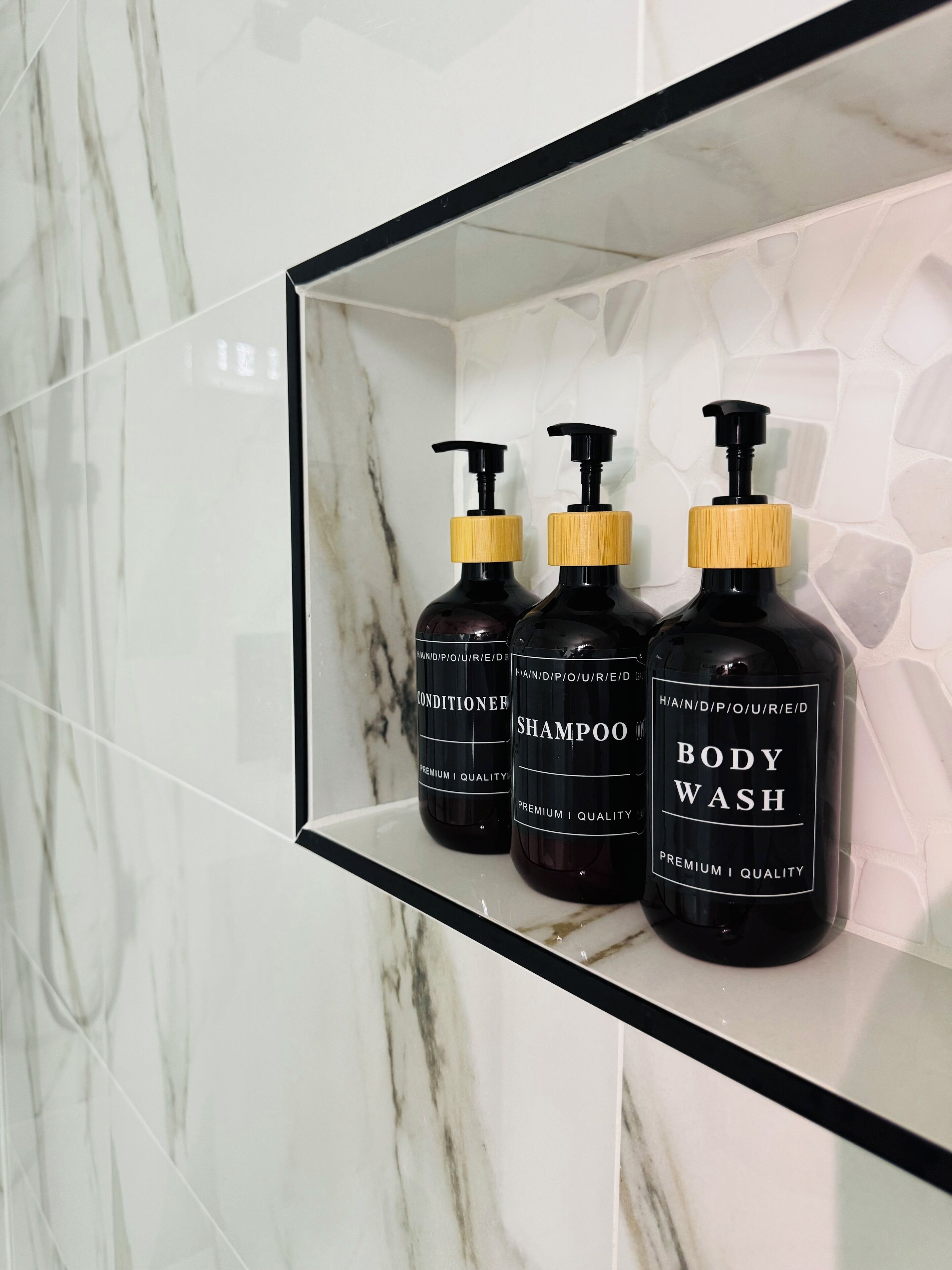 A bathroom shelf with three bottles of body wash, conditioner, and shampoo.
